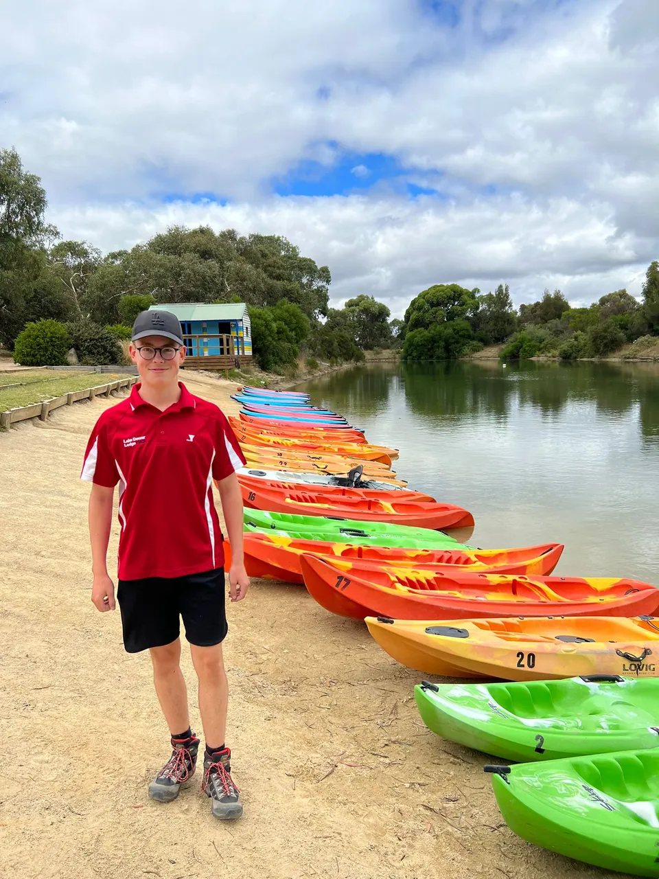 Participante frente a una fila de kayaks de colores junto a un lago en Australia