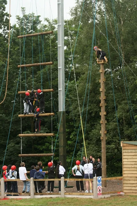 Escalera de cuerdas en altura con un grupo escolar esperando abajo